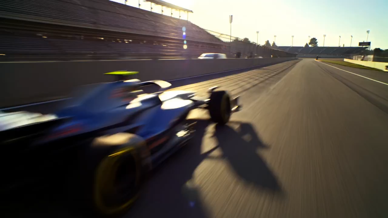 An F1 race car driver in full racing gear gripping the steering wheel inside the cockpit, the car screaming down the straight at blistering speed, heat haze shimmering off the sun-baked asphalt, motion blur streaking the background as the engine roars, capturing the raw intensity of Formula 1 racing with cinematic shallow depth of field